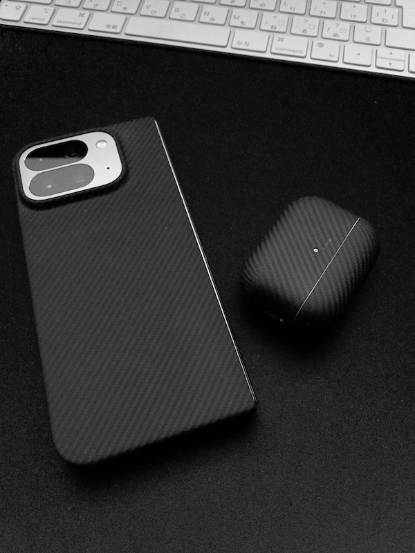 アラミド繊維製の保護ケースを装着したスマートフォンとAirPodsの充電ケースを並べた写真。どちらも黒い炭素繊維のような織り目