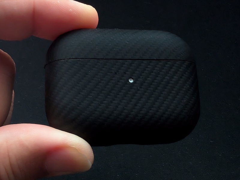 アラミド繊維製の保護カバーを装着したAirPods Proの充電ケースを手に持った様子。炭素繊維のような織り目のマットな質感